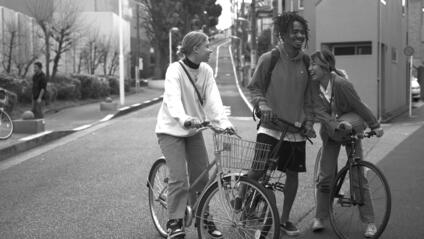 Three young people stand on bicycles in the street and laugh together.