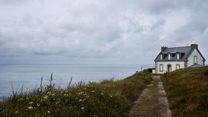 White house on a cliff, surrounded by flowers and a view of the cloudy sea.