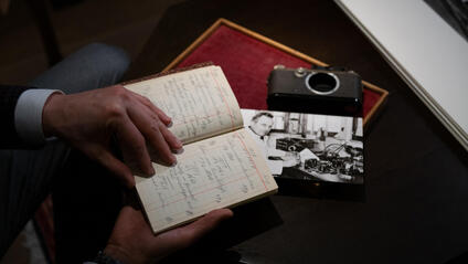 Person holding an old paper notebook, a photograph and a camera lie on the table.