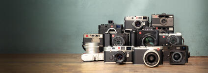 Vintage and new Leica cameras stacked on a wooden table