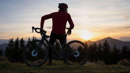 Man leaning on his mountain bike looking at the mountains at sunset.