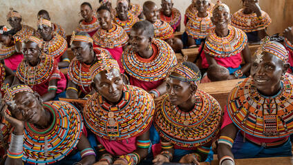 Women from the Samburu tribe in Kenya sitting on a wooden bench in traditional clothes and smiling.