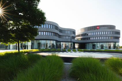 Leica building with glass facade and planted courtyard on sunny day.