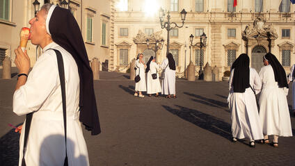 A nun eats an ice cream while several nuns talk in the background.