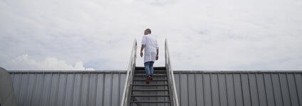 A man walks up a staircase with a cloudy sky in the background.