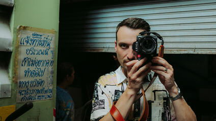 Philipp Reinhard looks through a camera and stands in front of a blue garage door.