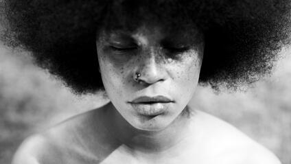 A close-up of a person with closed eyes and Afro hairstyle in black and white