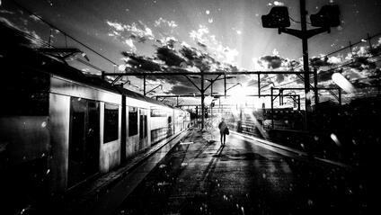 A person stands on a platform next to a train while the sun casts shadows.