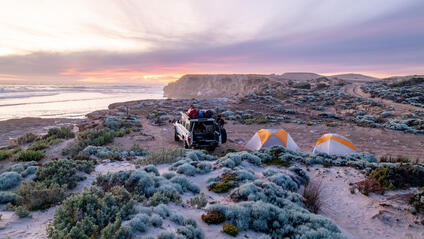 A jeep and two tents on a coast at sunset.