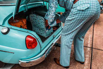 A person packs suitcases into the trunk of a turquoise vintage car.