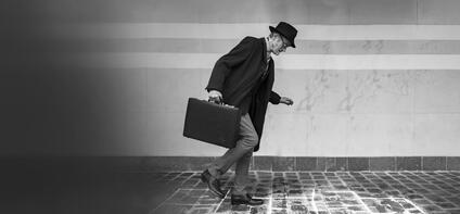 Elderly man in suit with hat and briefcase walking on icy cobblestones.