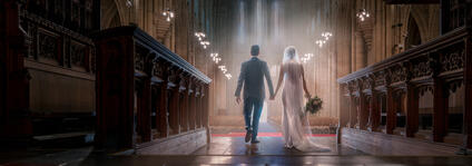 A bride and groom walk hand in hand down the aisle of an impressive church.