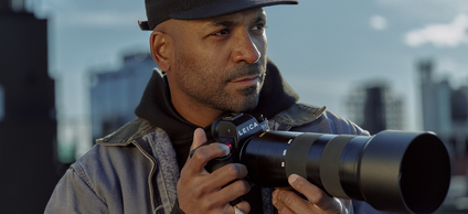 Close-up of a man holding a camera with skyscrapers in the background.