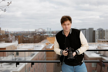 Person holding a camera, in the background are skyscrapers and a bridge on a cloudy day.