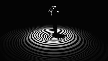 A single person with a hat stands in the centre of concentric circles on a dark background