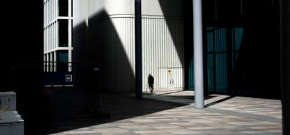 An old man walks in front of a building with shadows beside him.