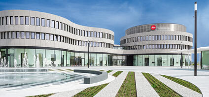 Modern architecture with Leica logo and curved glass facades and a fountain in front of the building.