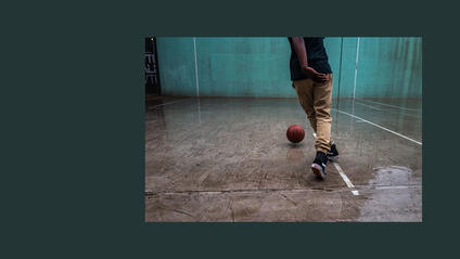 Person playing basketball on a wet court with a turquoise wall in the background.