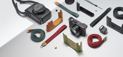 Leica camera with various straps, protective covers and accessories on a light background.