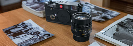 On the table are a camera, a camera lens and several stacks of black and white pictures.