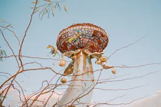 Metallic sculpture with colourful details in front of a blue sky and branches.