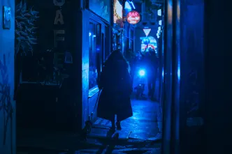 Person walking a dog through a narrow alley at night, illuminated by blue neon lights.