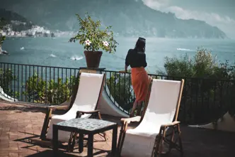 Woman on a large balcony with a view of a lake and mountains.