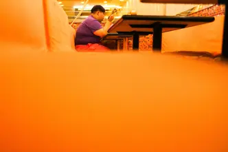 Close-up of an orange bench in a restaurant with a person sitting and eating in the background.