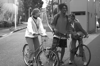 Three young people stand on bicycles in the street and laugh together.