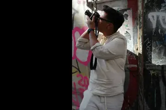 Patrick Domingo takes a photo standing in front of a graffiti wall.