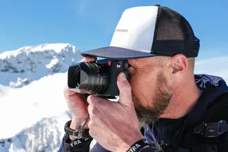 A man takes a photograph in a snowy mountain landscape.