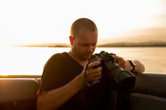 Tino Scherer looking at his camera. In the background is a sea at sunset.