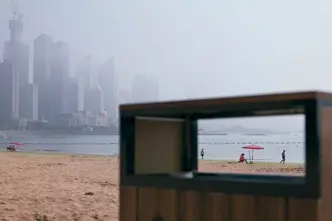 View through the rectangular opening of a garbage can on the beach with skyscrapers in the foggy background.