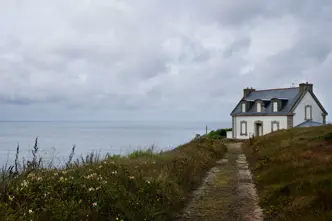 White house on a cliff, surrounded by flowers and a view of the cloudy sea.