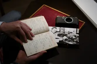 Person holding an old paper notebook, a photograph and a camera lie on the table.