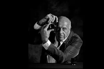 Elderly man holds a camera in front of his face and turns the lens of the camera.