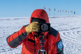 Person takes a photo in a snowy landscape with European flags in the background.
