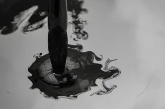 Brush dips into dark ink that spreads in the water.