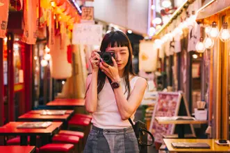 A woman takes pictures with a camera in a colorful, illuminated street.
