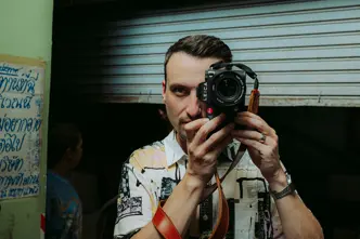 Philipp Reinhard looks through a camera and stands in front of a blue garage door.