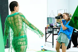 Photographer takes a picture in a studio of a model in a green net outfit.