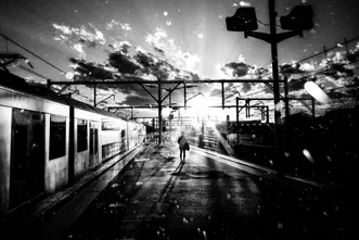 A person stands on a platform next to a train while the sun casts shadows.