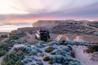 A jeep and two tents on a coast at sunset.