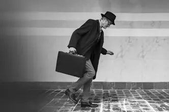 Elderly man in suit with hat and briefcase walking on icy cobblestones.