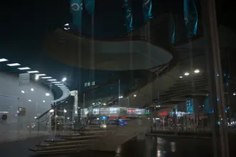 Reflection of a spiral staircase and a city at night in the glass front of a building.