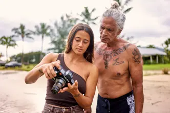 Mainei Kinimaka shows pictures on a camera to a man with Hawaiian tattoos on his upper body