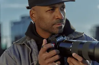 Close-up of a man holding a camera with skyscrapers in the background. 