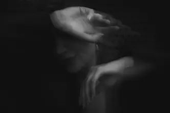 Blurred black and white image of a person covering her face with her arm.