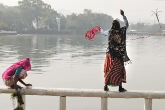 A woman and a child are standing on a railing in front of a lake and are fishing.