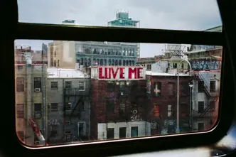View from a window of a city with a building bearing the graffiti ‘LOVE ME’.